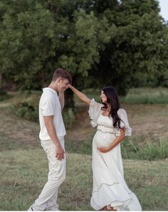 a pregnant couple standing in the grass with their hands on each other's forehead