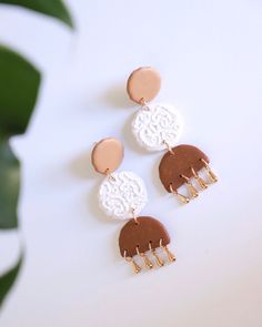 three pairs of earrings on top of a white table next to a potted plant