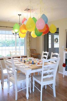 a dining room table with many balloons hanging from it's centerpieces over it