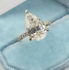 an engagement ring with a pear shaped diamond on top in a blue velvet box,