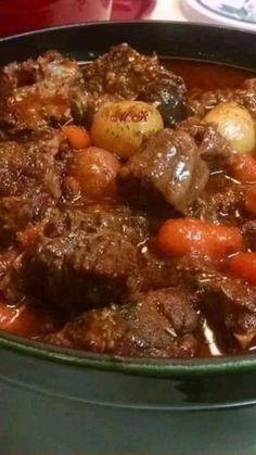 beef stew with carrots and potatoes in a green pot on the stove top, ready to be eaten