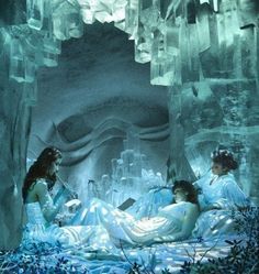 two women sitting on the ground in front of an ice cave