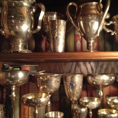 many silver cups and vases are sitting on a shelf in front of some books