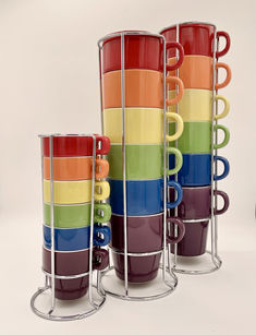 four multicolored coffee cups are stacked in a row with metal holders on each side