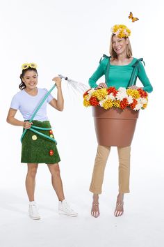 two women in flowerpots with flowers and gardening equipment on their heads, one holding a watering hose