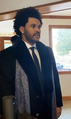 a man wearing a suit and tie standing in front of a window