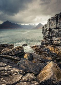 some rocks and water with mountains in the backgroung on an overcast day