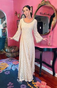 a woman standing in front of a mirror wearing a long white dress with bell sleeves