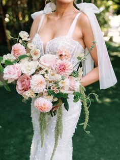 a woman in a wedding dress holding a bouquet of pink and white flowers with greenery