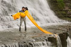 a man and woman are standing in front of a waterfall with an orange scarf around their necks