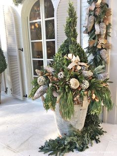 a large potted plant with pine cones and greenery in front of a house