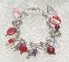 You'll sparkle with this one-of-a-kind charm bracelet.  Nineteen handcrafted charms in shades of red, pink, and silver silver dangle from handcrafted silver-tone links. Bracelet measures 7½" long and has a magnetic clasp for easy one-handed closure. Stock #7522-0123 Red Dangle Charm Bracelet As Gift, Handmade Red Metal Bracelets, Red Dangle Charm Bracelet For Gift, Red Nickel-free Metal Bracelet, Nickel-free Red Metal Bracelet, Nickel-free Red Beaded Bracelet As Gift, Red Nickel-free Metal Bracelets, Nickel-free Red Metal Bracelets, Red Metal Charm Bracelet