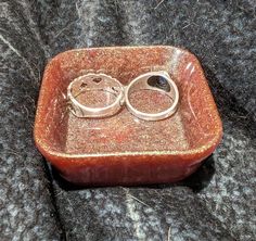 two wedding rings are placed in a red dish on a black surface with silver flecks