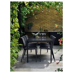 an outdoor dining table with four chairs and two wine glasses on it in front of a brick wall