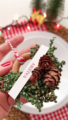 a person holding a small pine cone on top of a white plate next to a christmas tree