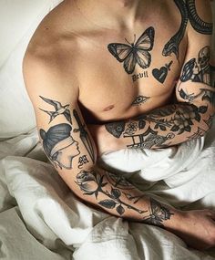 a man with tattoos on his arm and chest laying in bed next to white sheets