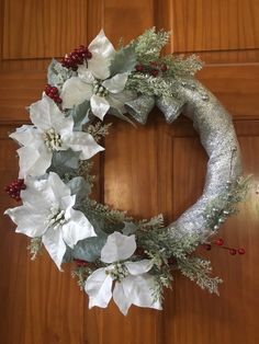 a wreath with white poinsettis and greenery hanging on a wooden door