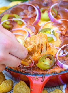 a person dipping some food into a red pan with onions and peppers on it,