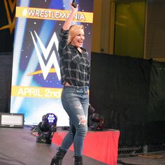 a woman in black shirt and jeans standing on stage with her arms up to the sky