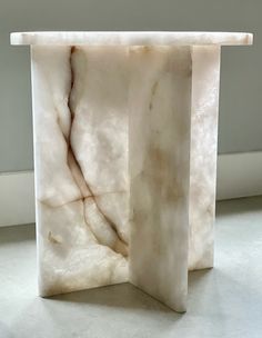 a white marble table with a square base on the floor in front of a wall