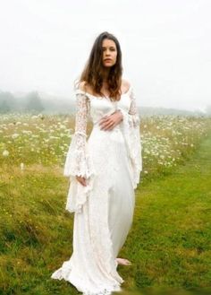 a woman standing in a field wearing a white dress and holding her hands on her hips