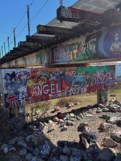 graffiti on the side of an old bridge over rocks and gravel in front of a body of water