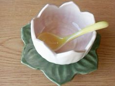 a spoon in a small bowl on top of a green leaf shaped plate with a yellow liquid pouring into it