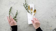 two hands holding forks and knives on top of a white marble table with gold utensils