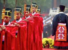 men dressed in traditional chinese garb and headdresses are marching down the street