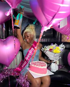 a woman sitting in front of a cake and balloons