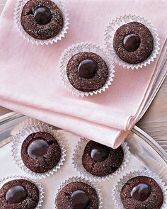 four chocolate cupcakes sitting on top of a glass plate next to a pink napkin