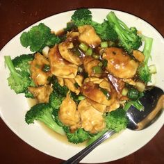 a white plate topped with chicken and broccoli covered in sauce next to a spoon