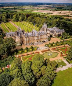 an aerial view of a large building surrounded by trees and grass in the middle of a park