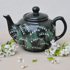 a black teapot with white flowers and leaves on the table next to it's lid