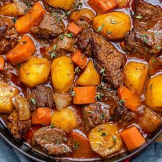 beef stew with carrots and potatoes in a skillet on a blue cloth next to a wooden spoon