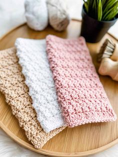 three crocheted dishcloths sitting on top of a wooden tray next to a potted plant