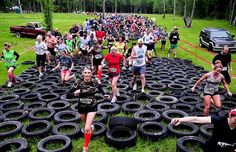 a group of people are running through an obstacle course with tires on the ground in front of them