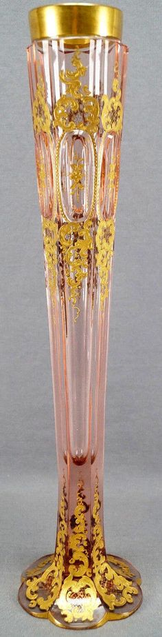 a pink glass vase with gold trimmings on the bottom and sides, in front of a gray background