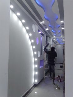 a man standing on a ladder in front of a white wall with blue and purple lights