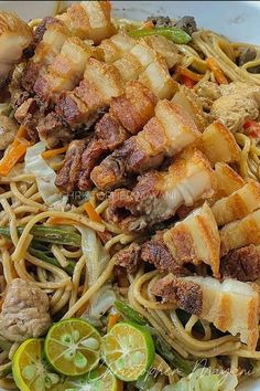 a white bowl filled with noodles, meat and veggies next to lemon wedges