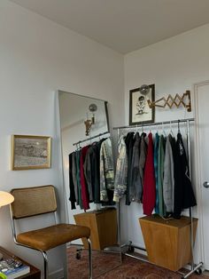 a closet with clothes hanging on the wall and a chair next to it in front of a mirror