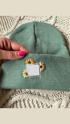 a woman's hand holding onto a green beanie hat with flowers on it