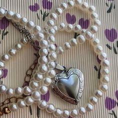 a necklace with pearls and a heart shaped locke attached to it on top of a table