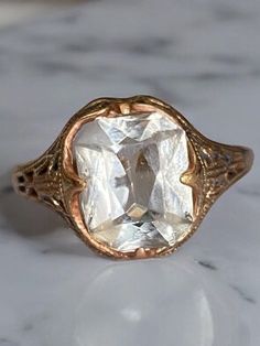 an antique style ring with a large white stone in the center on a marble surface