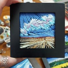 a person holding up a small frame with some art on it