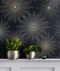 two potted plants sit on a mantle in front of a wallpapered background