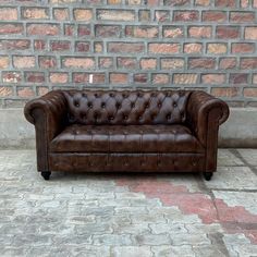 a brown leather couch sitting in front of a brick wall