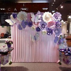 a pink and purple backdrop with paper flowers on it at a wedding reception or event