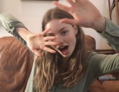 a young woman is holding her hands up in the air while sitting on a couch