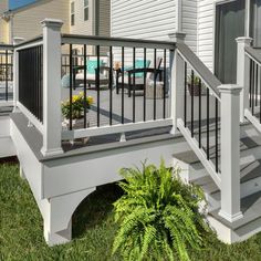 a white deck with black railing and planters on the grass next to it in front of a house